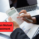 Person using a calculator to plan mutual fund investment with financial charts and laptop for investment planning.