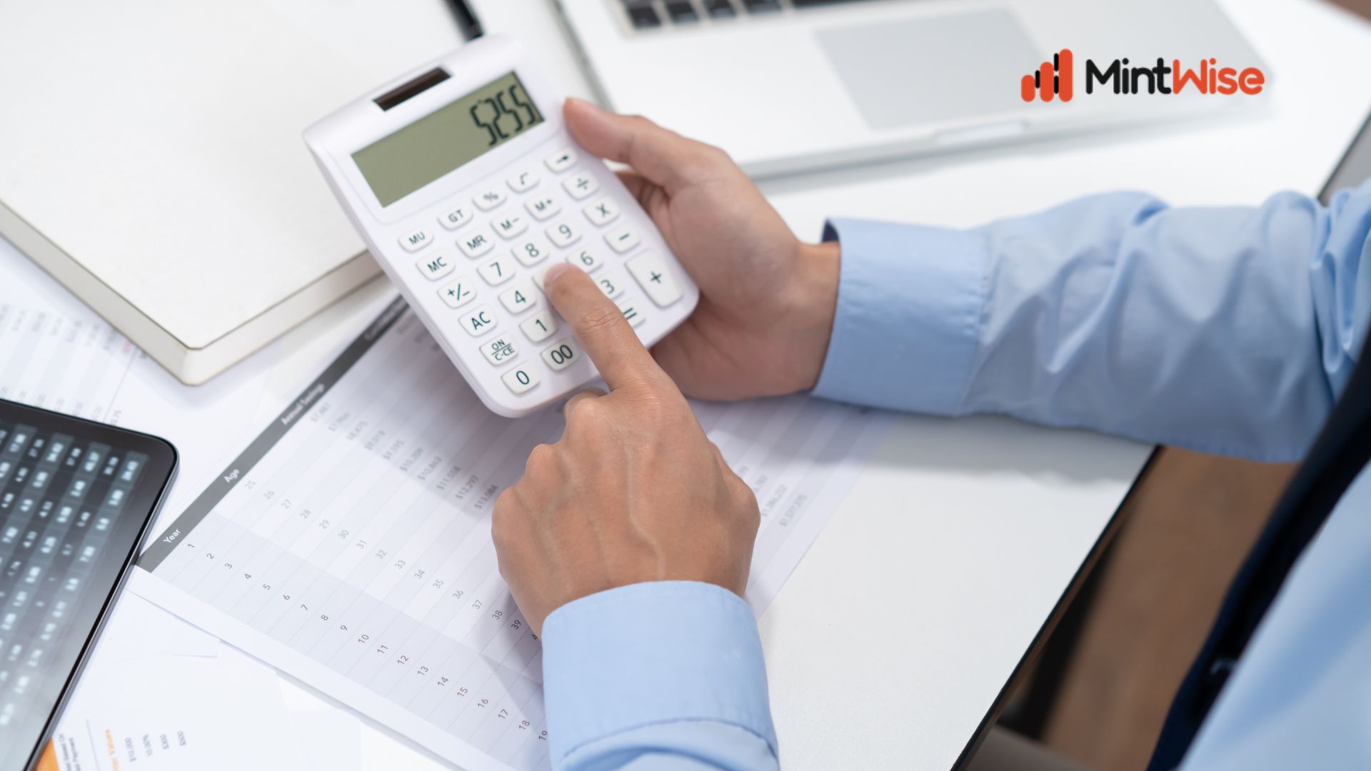 MintWise Business Planning Savings Tool showing a professional using a calculator, financial documents, and a laptop to estimate business savings, budget planning, and financial forecasting.